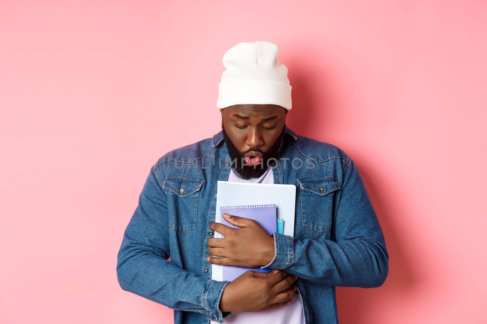 Education. Image of african-american bearded male student holding notebooks and looking down, drop something on floor, standing over pink background.