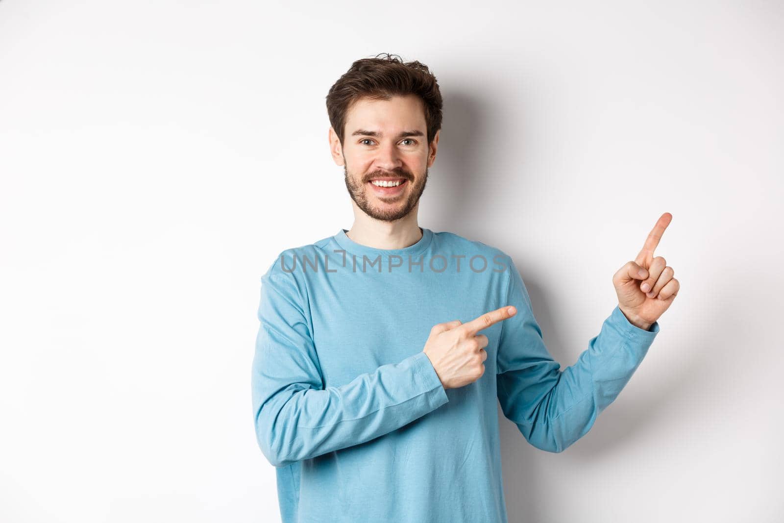 Happy bearded man showing advertisement, pointing fingers right and smiling, inviting to click link, standing over white background.