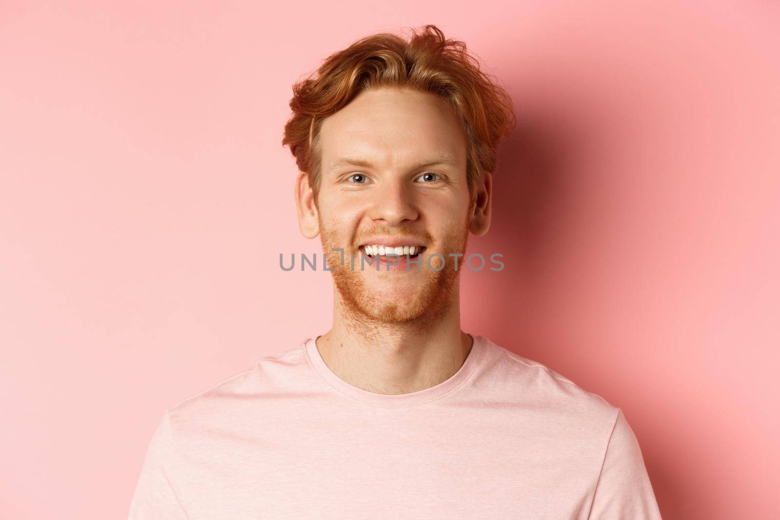 Headshot of happy redhead man with beard and white teeth, smiling excited at camera, standing over pink background by Benzoix