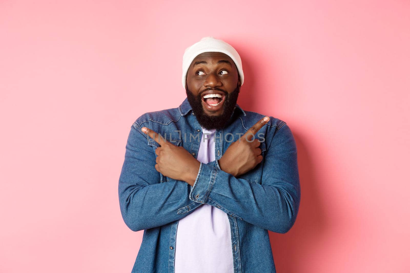 Excited young african-american man pointing sideways, showing two choices and making decision, smiling happy, standing over pink background.