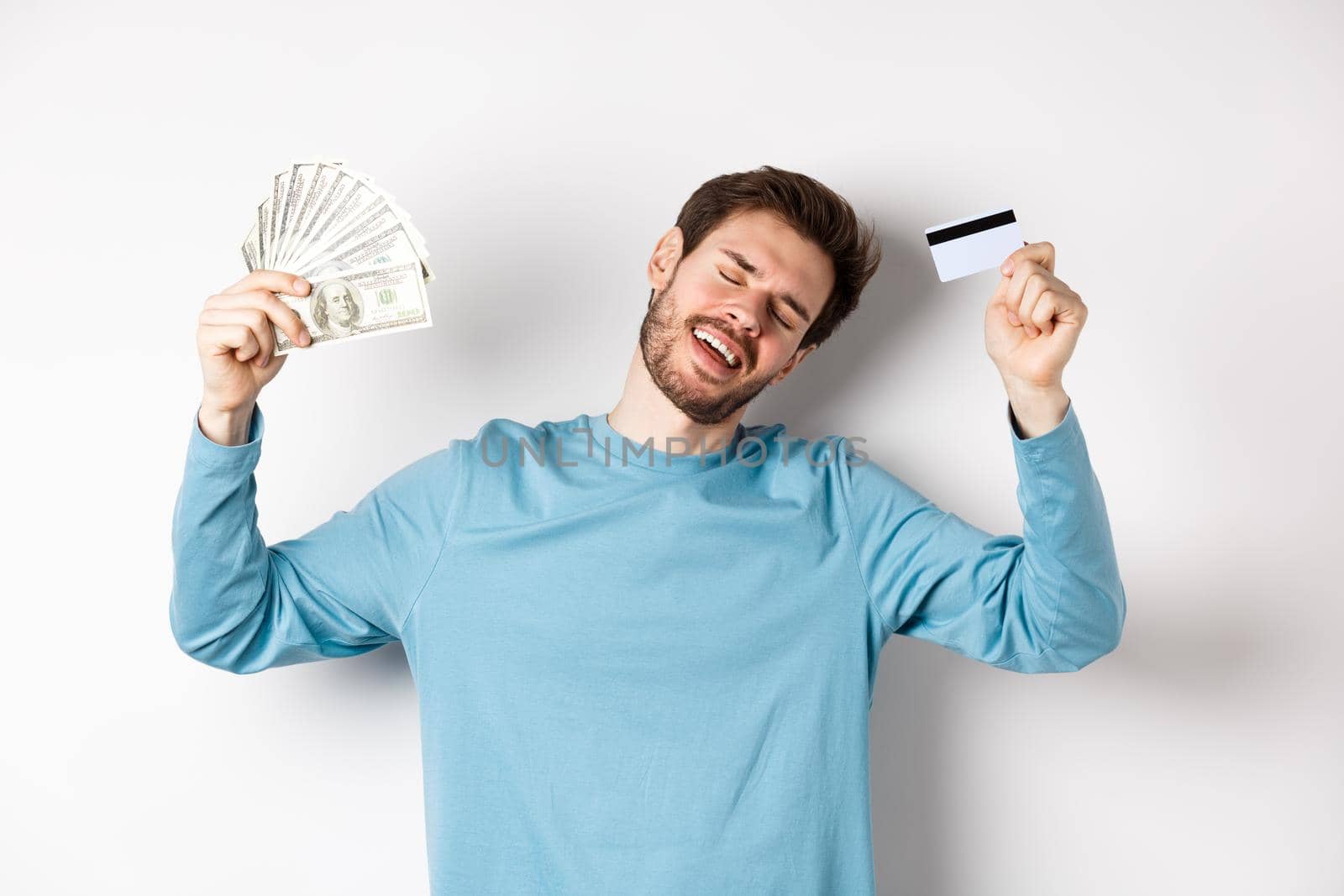 Handsome man dancing with money and plastic credit card, standing in casual clothes over white background by Benzoix