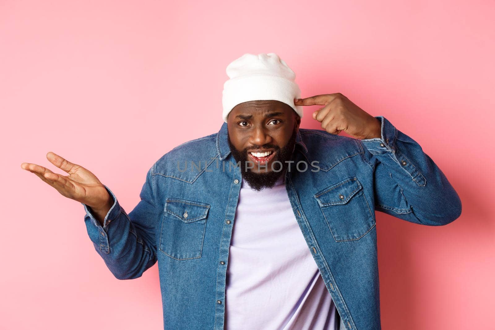 Annoyed and pissed-off african-american man pointing finger at head, scolding someone stupid, staring bothered at camera, pink background.