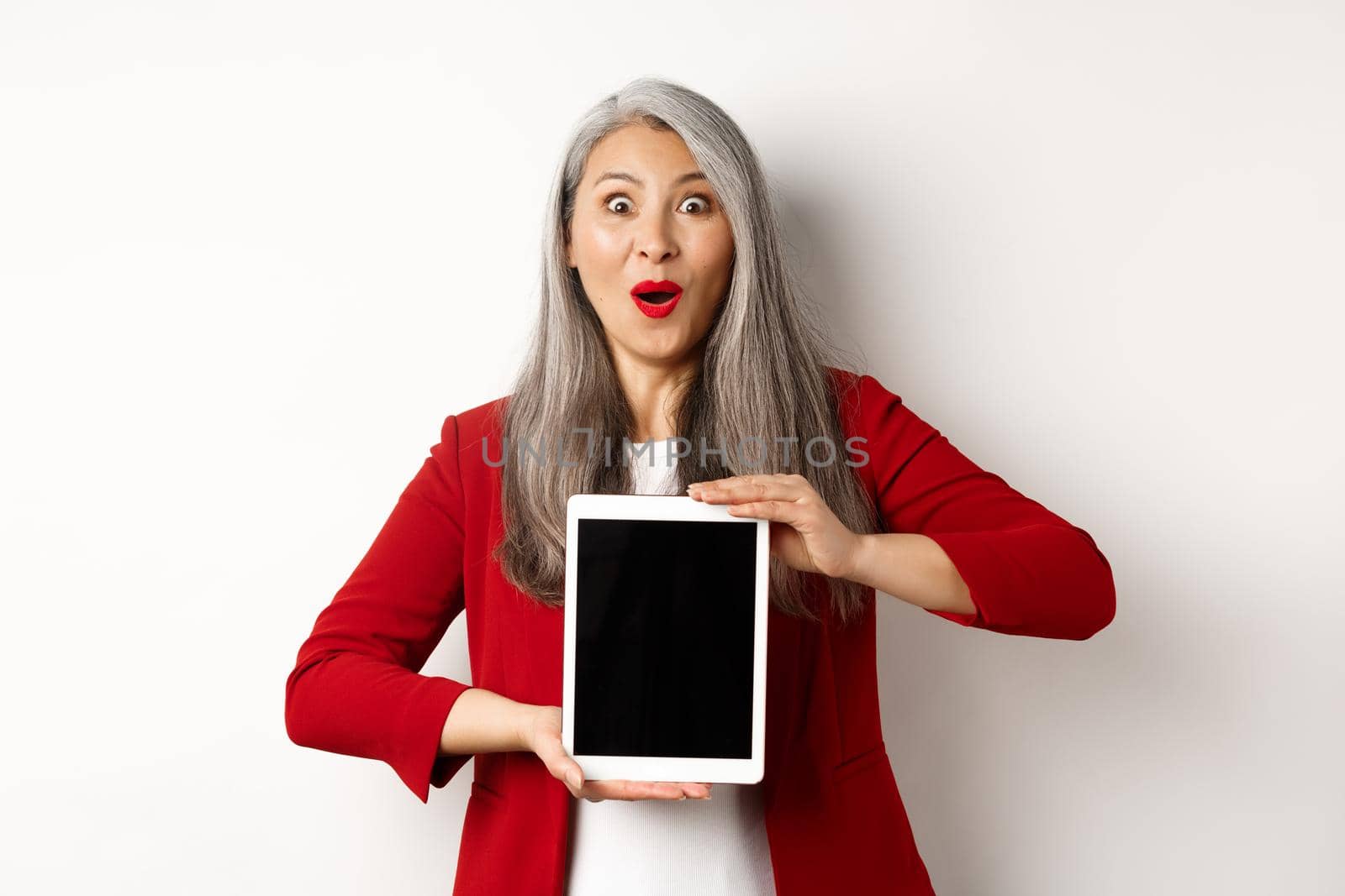 Business. Surprised and happy asian female entrepreneur showing promotion on blank digital tablet screen, staring at camera amazed, white background by Benzoix