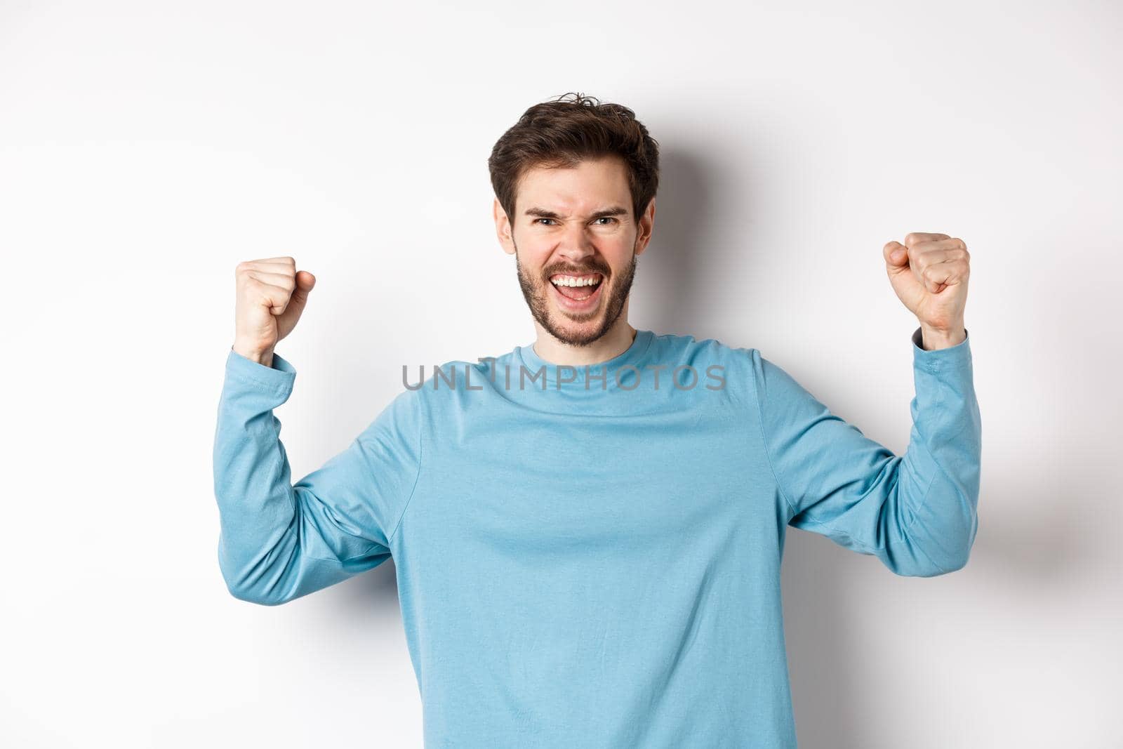 Portrait of satisfied handsome man winning prize, rejoicing in triumph, celebrating victory and shouting yes, standing over white background.