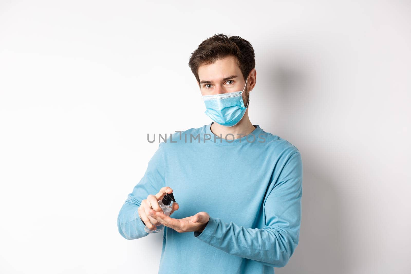 Covid-19, health and quarantine concept. Caucasian man in medical mask using hand sanitizer, apply antiseptic from coronavirus spread, white background by Benzoix