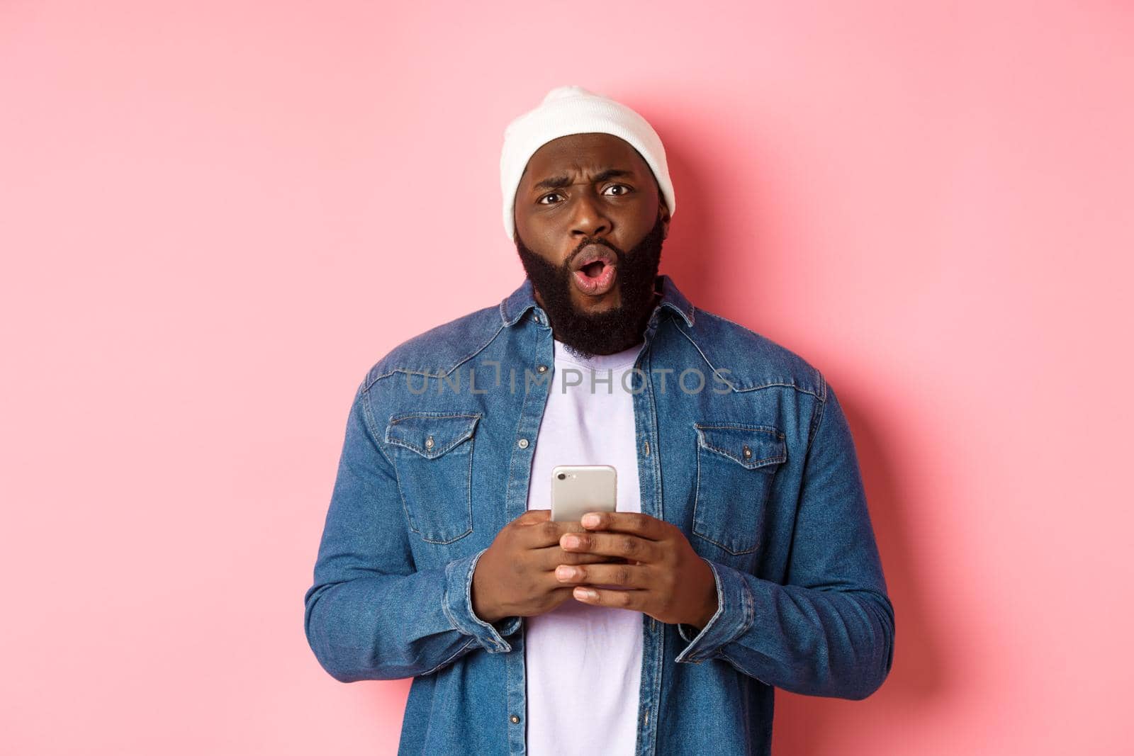 Technology and online shopping concept. Confused and disappointed african-american man complaining, holding mobile phone and staring at camera.