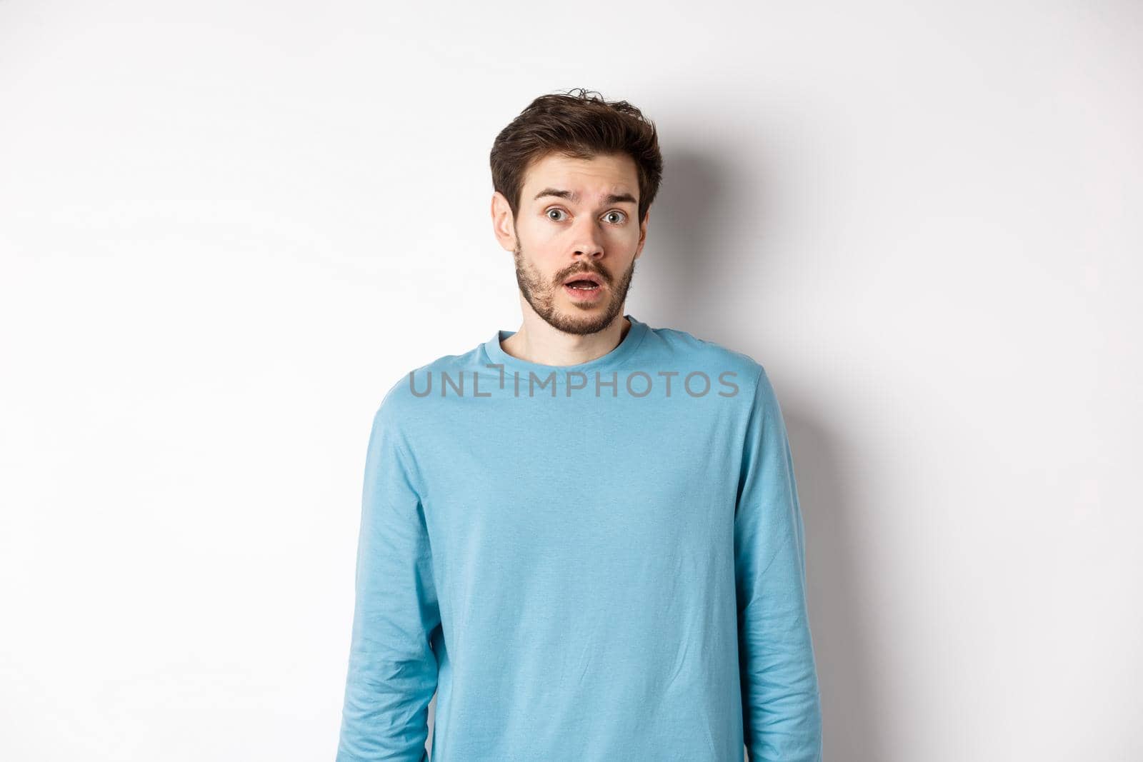Confused caucasian guy drop jaw and stare startled at camera, standing over white background by Benzoix