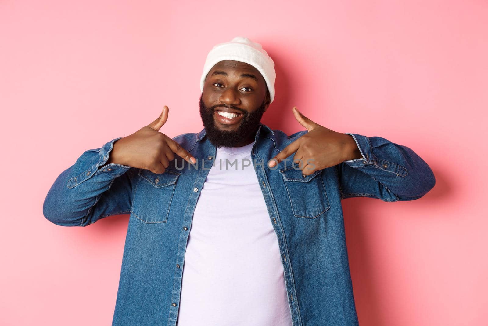 Happy young african-american hipster guy pointing at himself t-shirt, smiling pleased, standing over pink background.