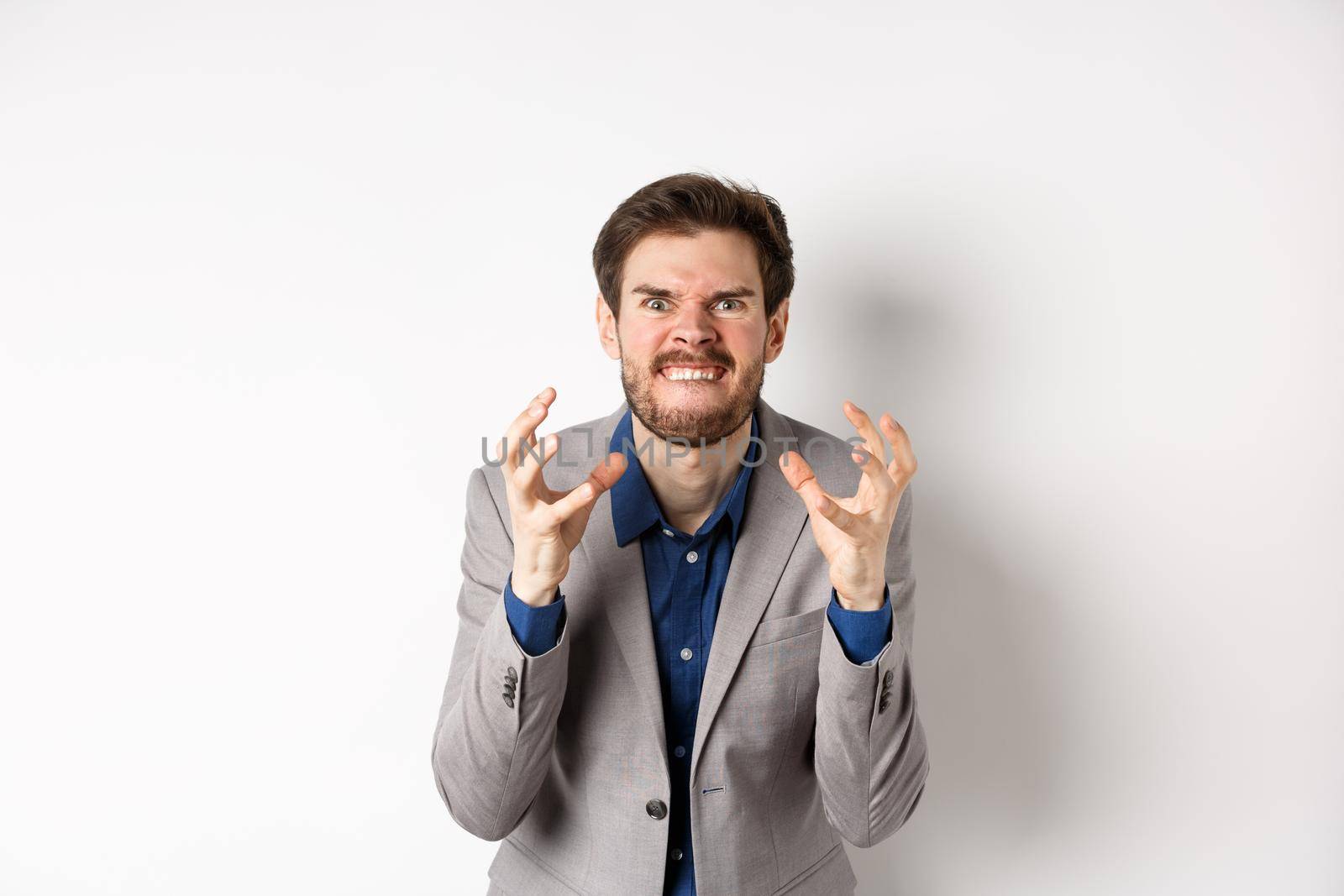 Angry and tensed businessman wants to kill someone, clenching hands and teeth, looking mad at camera, going to strangle person, standing on white background by Benzoix