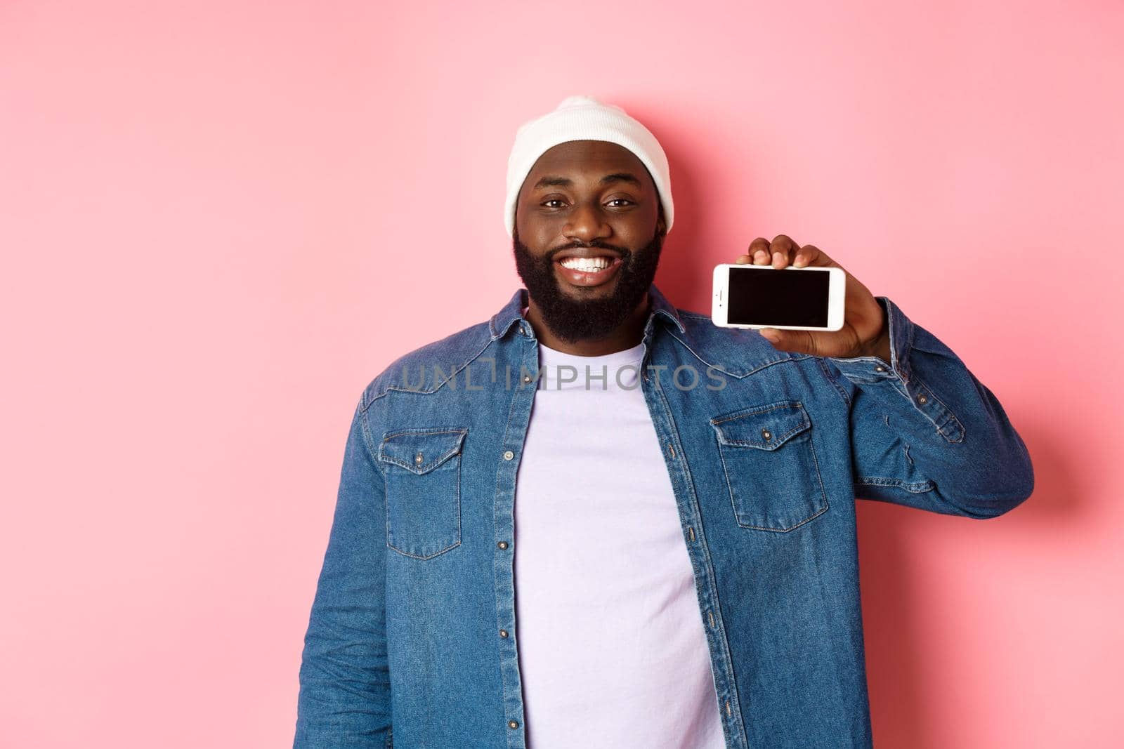 Online shopping and technology concept. Handsome Black man showing smartphone screen horizontally and smiling satisfied, recommending app, pink background by Benzoix