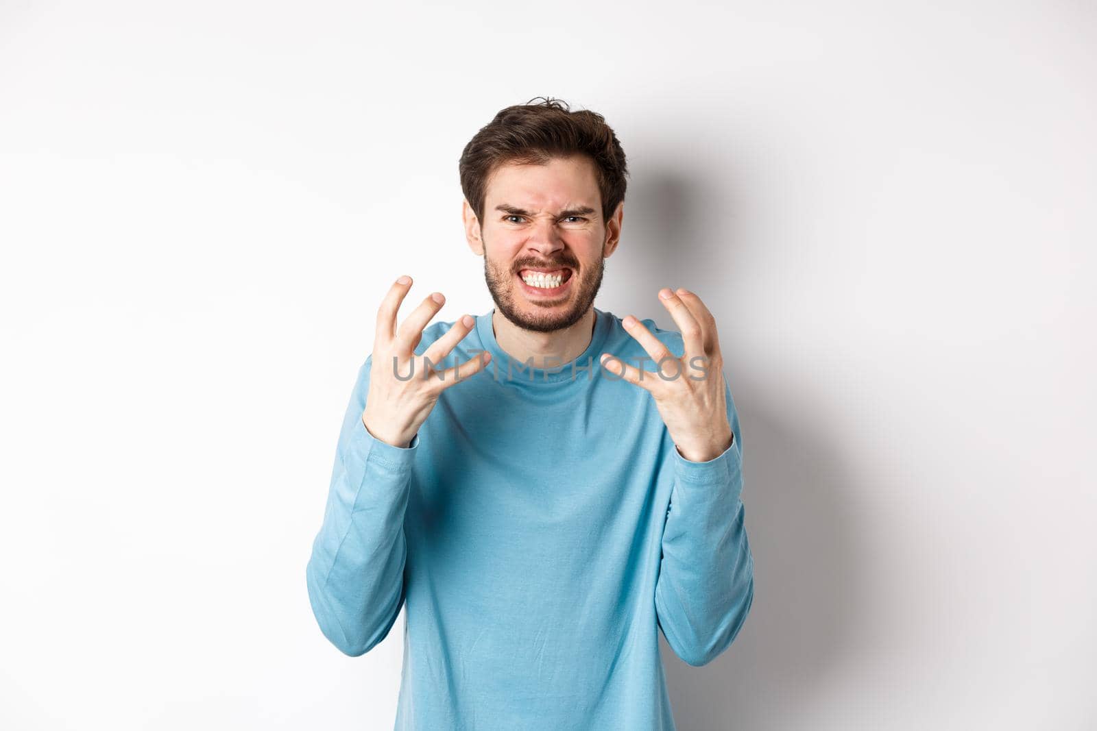 Angry caucasian man shaking hands and grimacing, looking with mad face, express hatred against white background. Copy space
