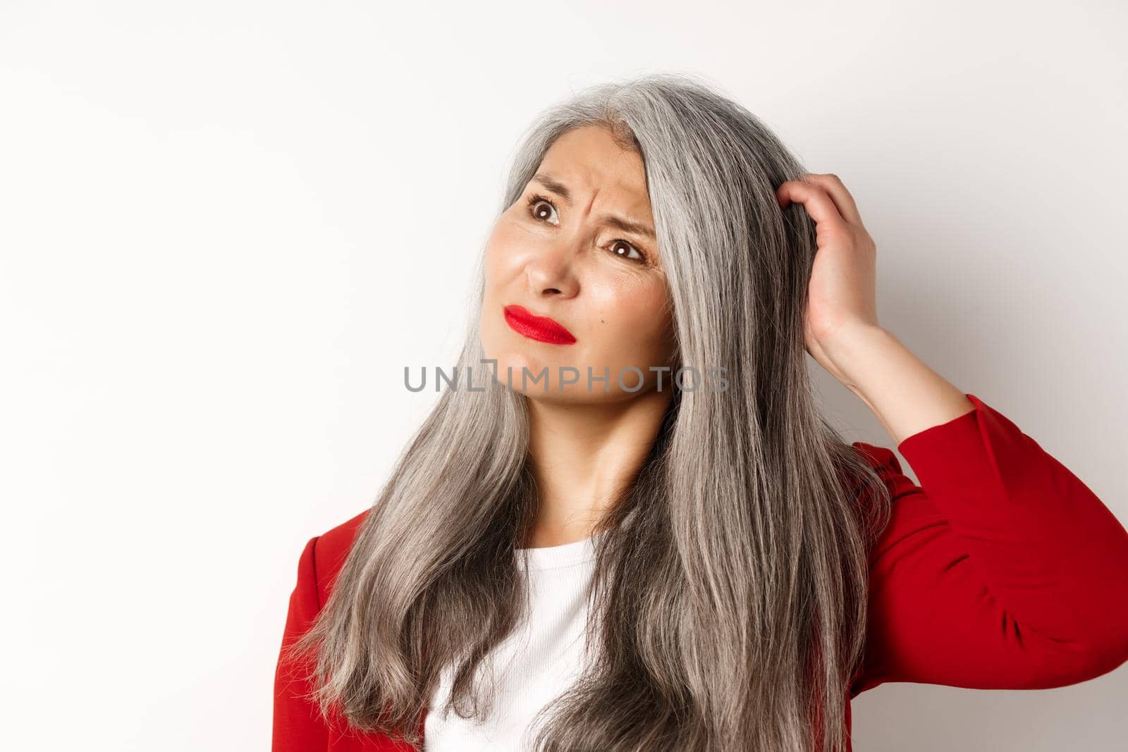 Close up of complicated asian mature woman scratching head, looking confused at upper left corner, standing and thinking over white background by Benzoix
