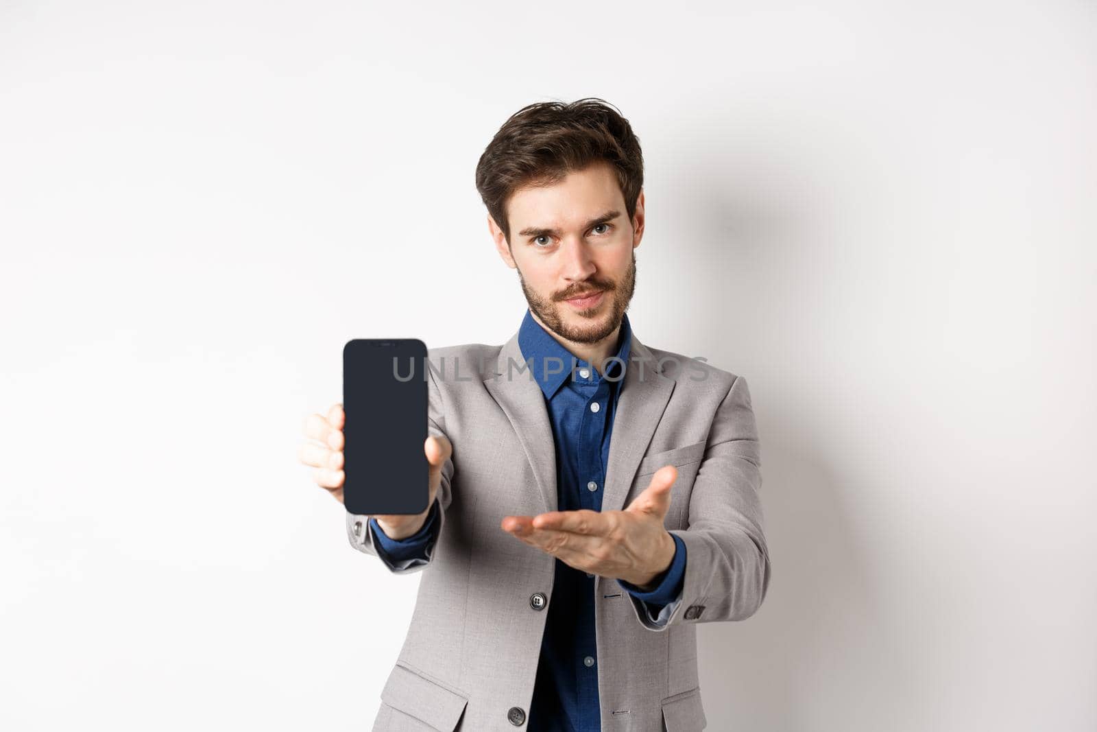 E-commerce and online shopping concept. Man demonstrated empty smartphone screen to you, showing phone display to introduce something, standing on white background.