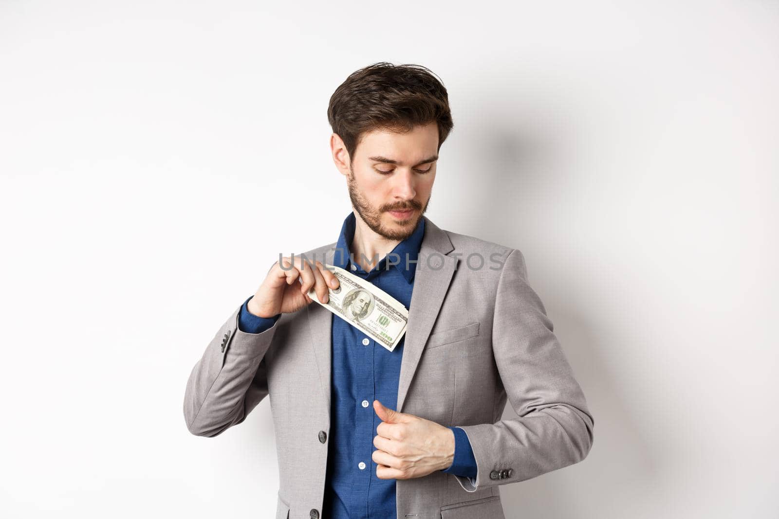 Successful businessman put dollars inside suit pocket, hiding money, standing on white background by Benzoix