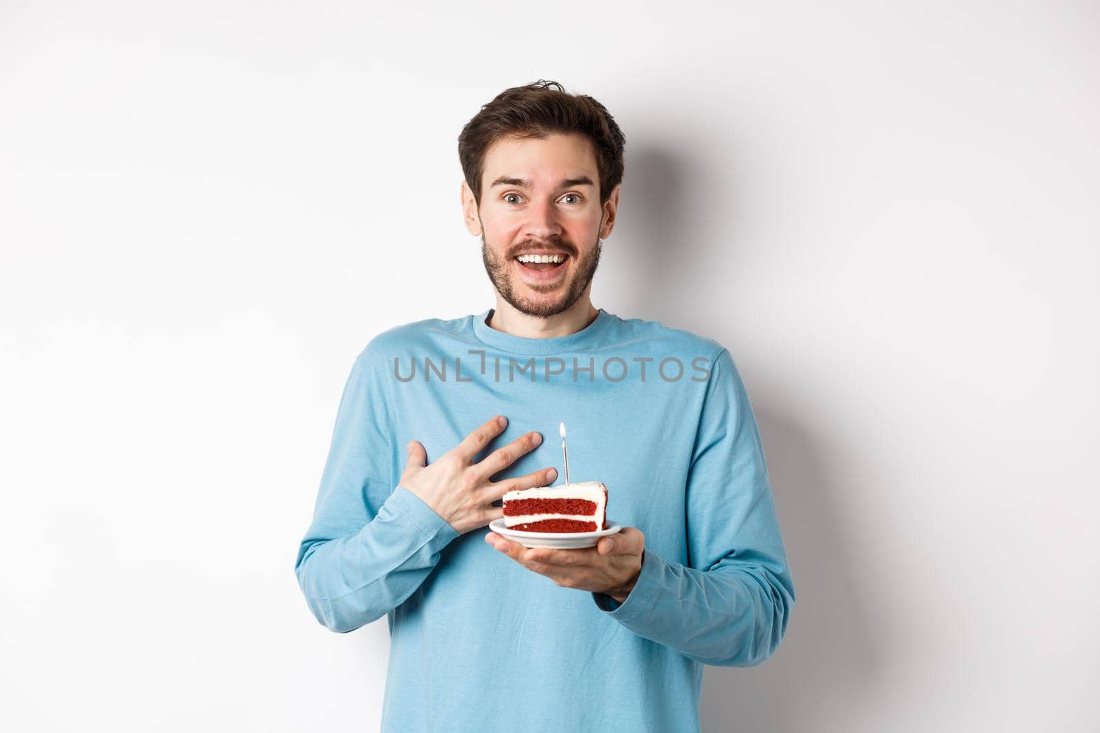 Surprised man receiving birthday cake with lit candle, being congratulated with b-day, gasping amazed, standing over white background by Benzoix