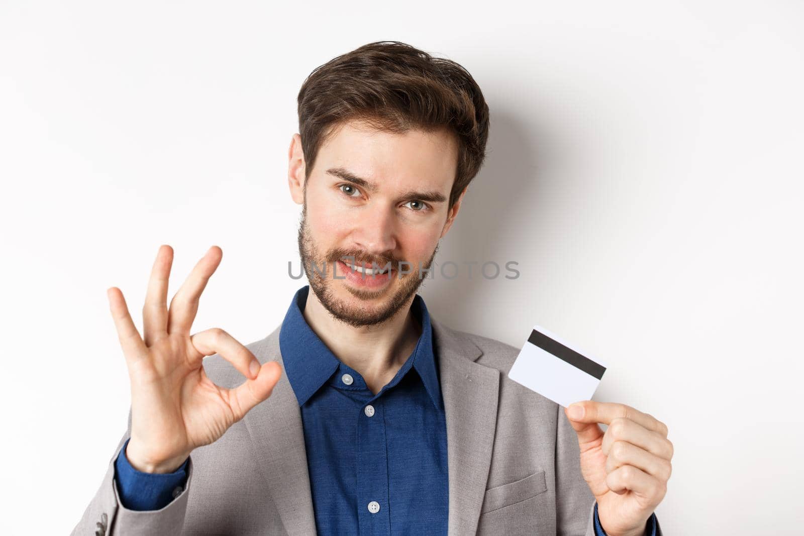 Shopping. Handsome man showing okay sign and plastic credit card, all under control, no worries gesture, white background.
