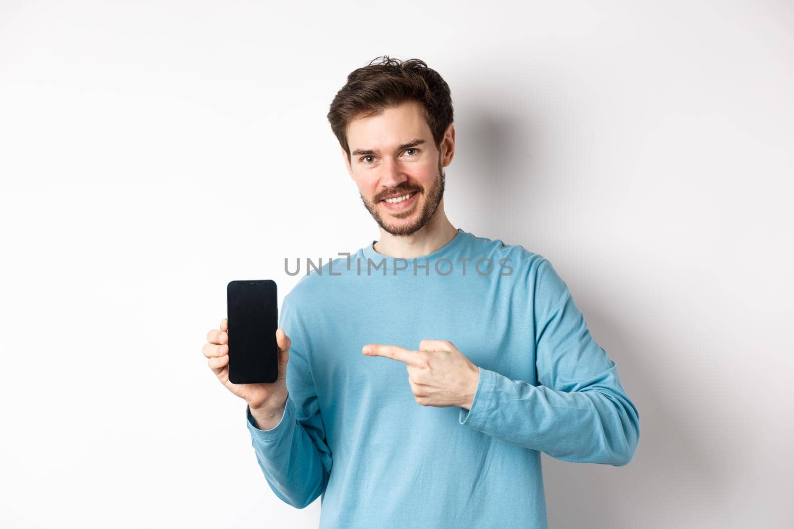 E-commerce and shopping concept. Smiling caucasian man pointing finger at empty smartphone screen, showing online offer, white background by Benzoix