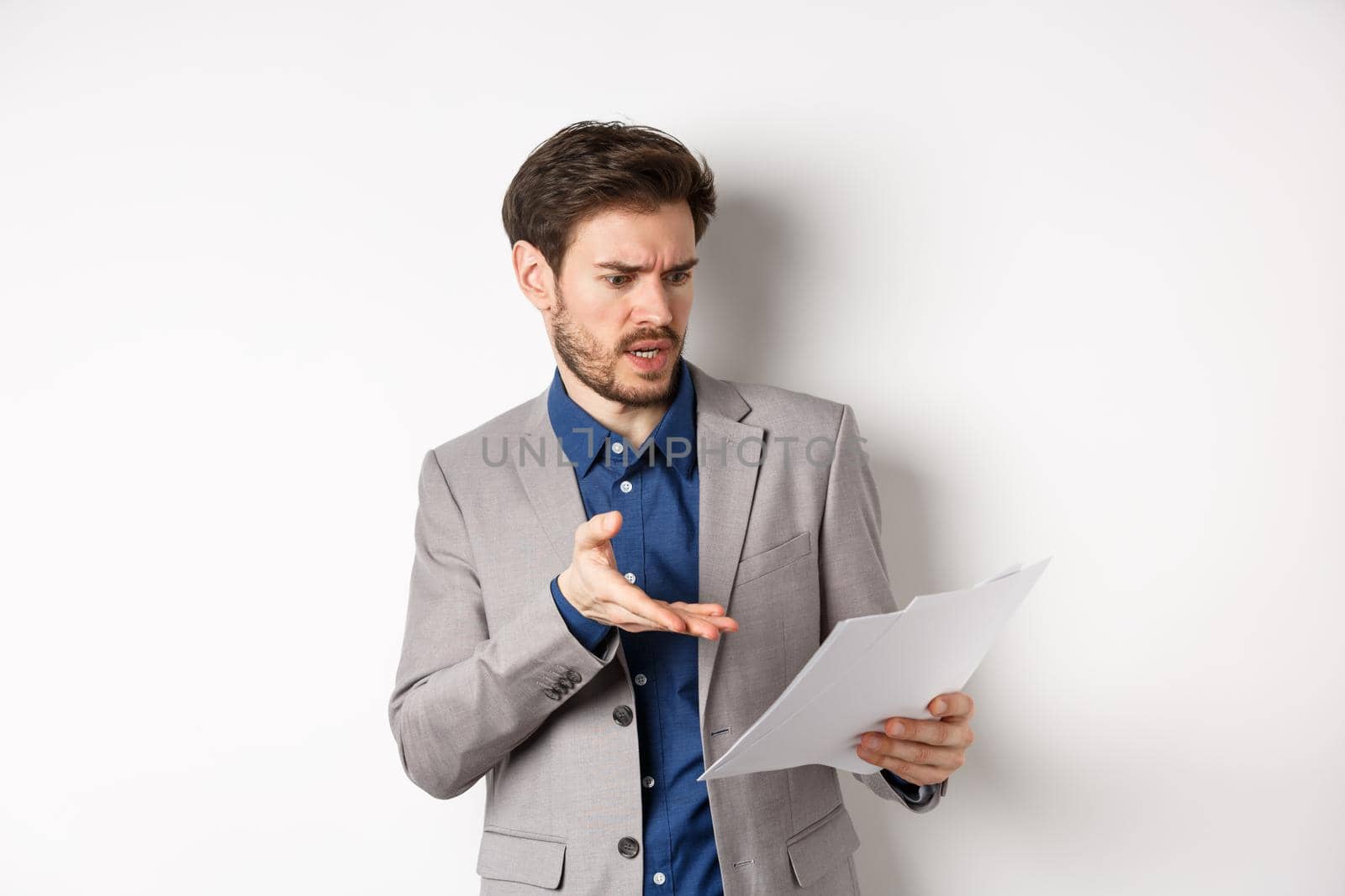Angry employer looking at bad document, complaining on deal, pointing at paper frustrated, standing in suit on white background.