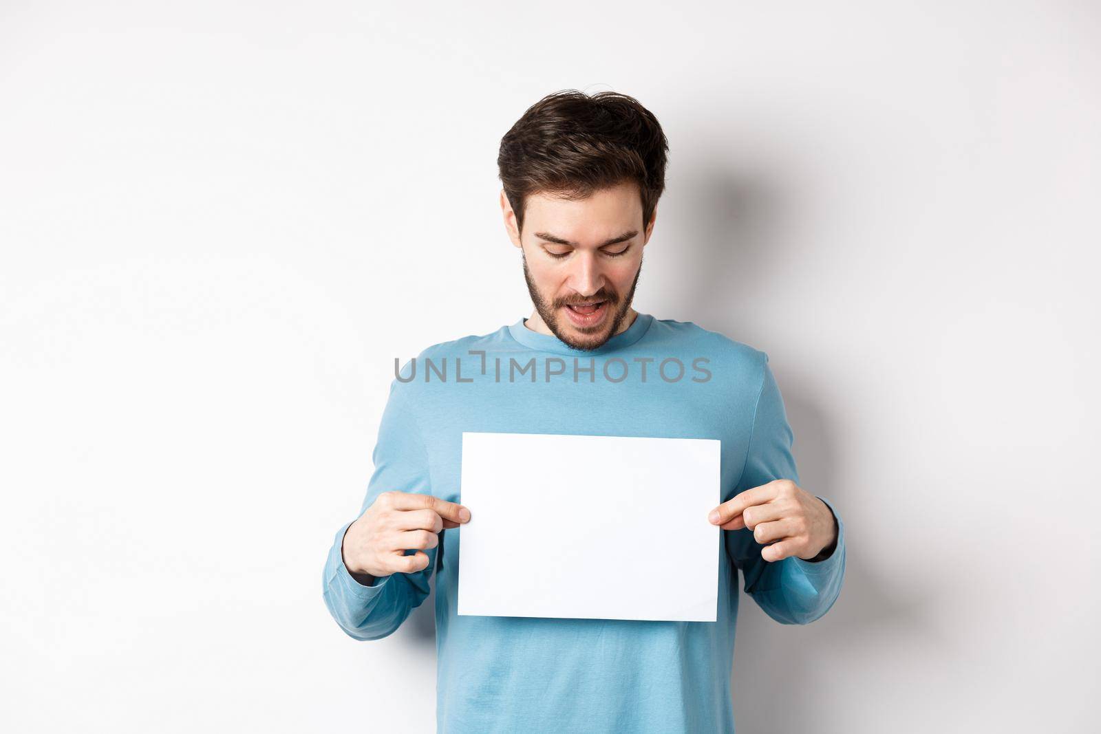 Excited bearded guy reading banner on blank piece of paper, showing logo, standing over white background by Benzoix