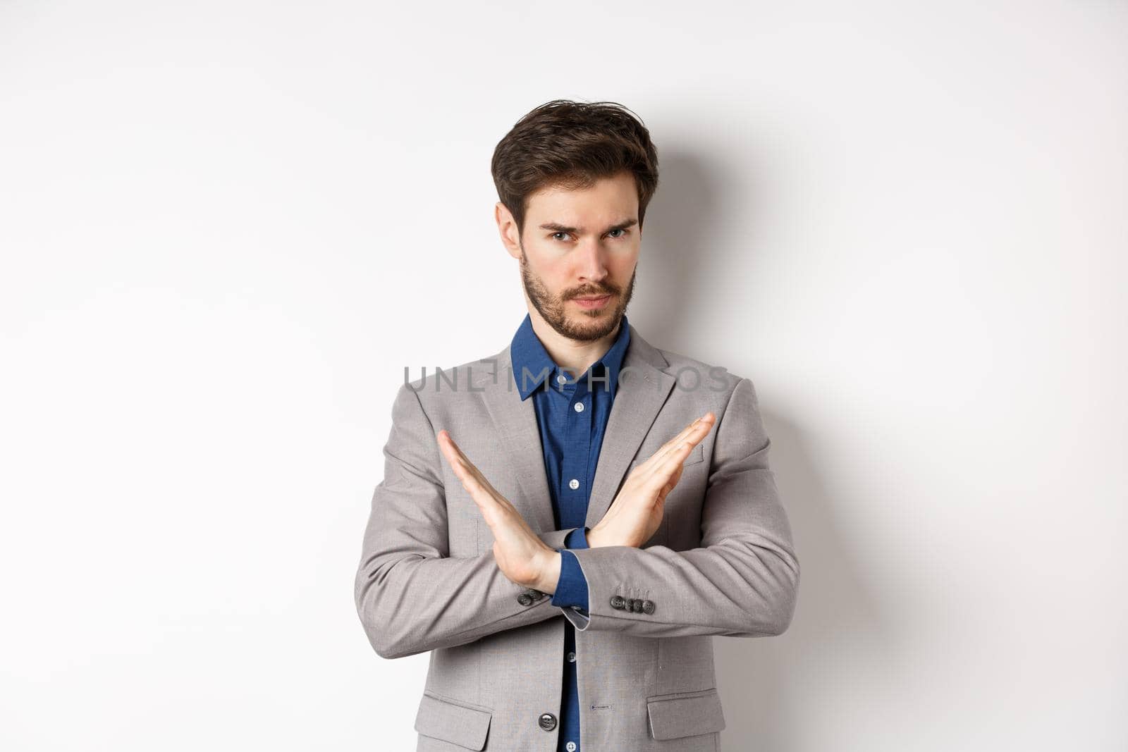 Serious business man making cross and says no, looking determined, disagree and prohibit something bad, tell to stop, standing in suit on white background.