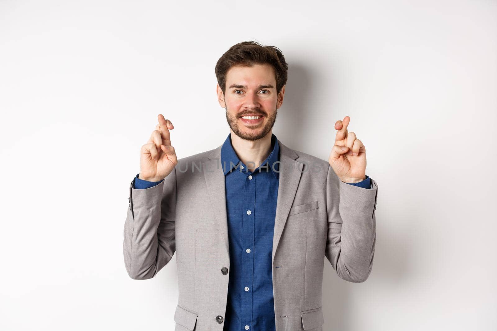 Hopeful smiling businessman looking optimistic, cross fingers good luck, praying to win, waiting for results with hope, standing on white background by Benzoix