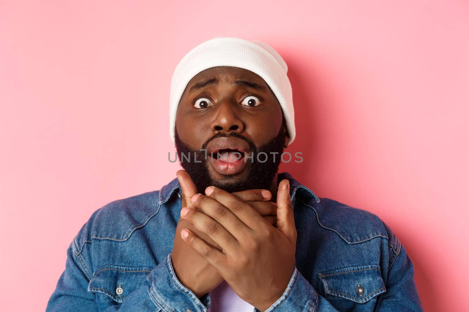 Shocked and scared african-american man staring at camera strtled, gasping concerned, standing over pink background.