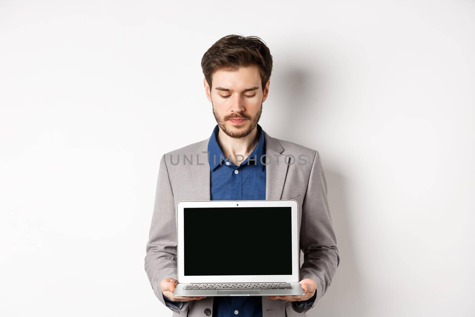 Handsome caucasian businessman in suit showing empty laptop screen, demonstrate promo, standing on white background.
