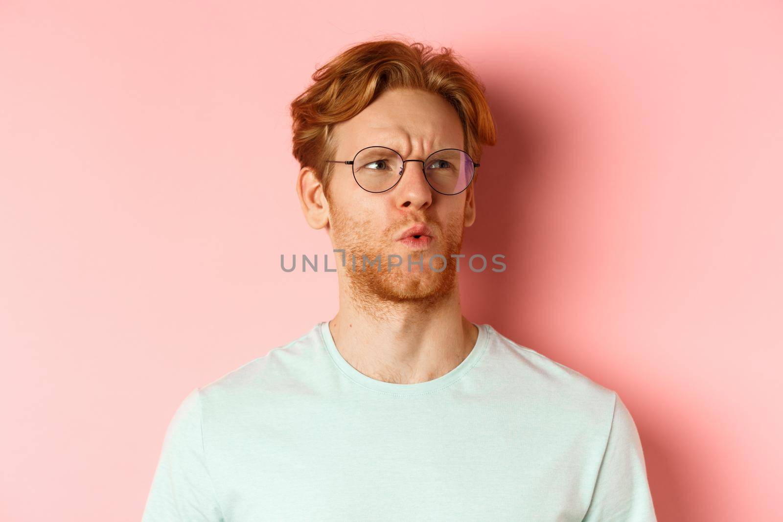 Ouch thats bad. Face of redhead man showing pity and feeling sorry for someone, frowning and looking with compassion, standing over pink background.