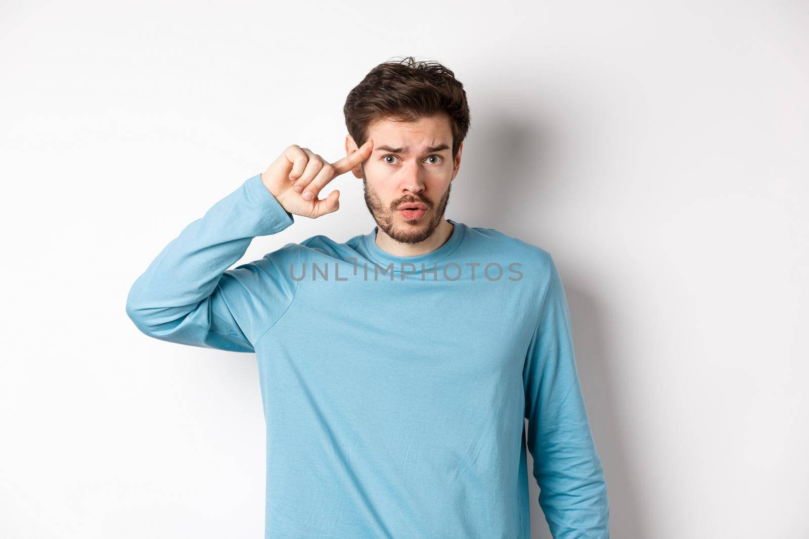 Annoyed caucasian man roll finger on temple, are you stupid or crazy gesture, scolding someone acting strange, standing in sweatshirt over white background.