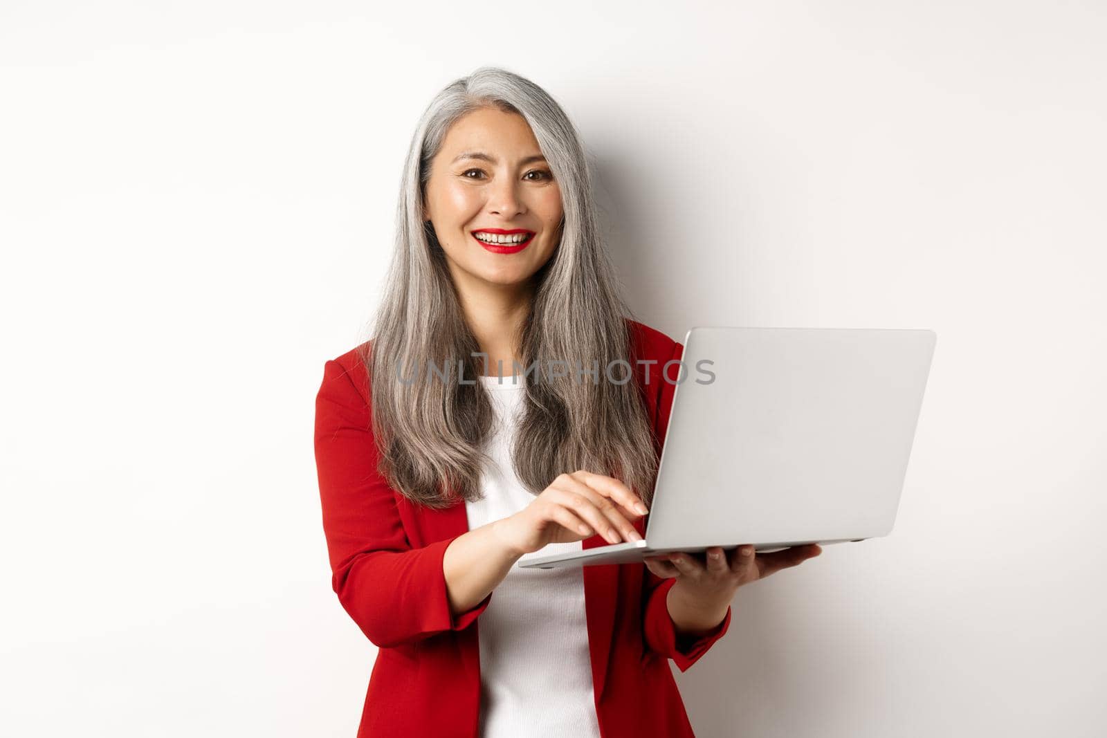 Business. Senior woman working on laptop, wearing office outfit and smiling, standing over white background.