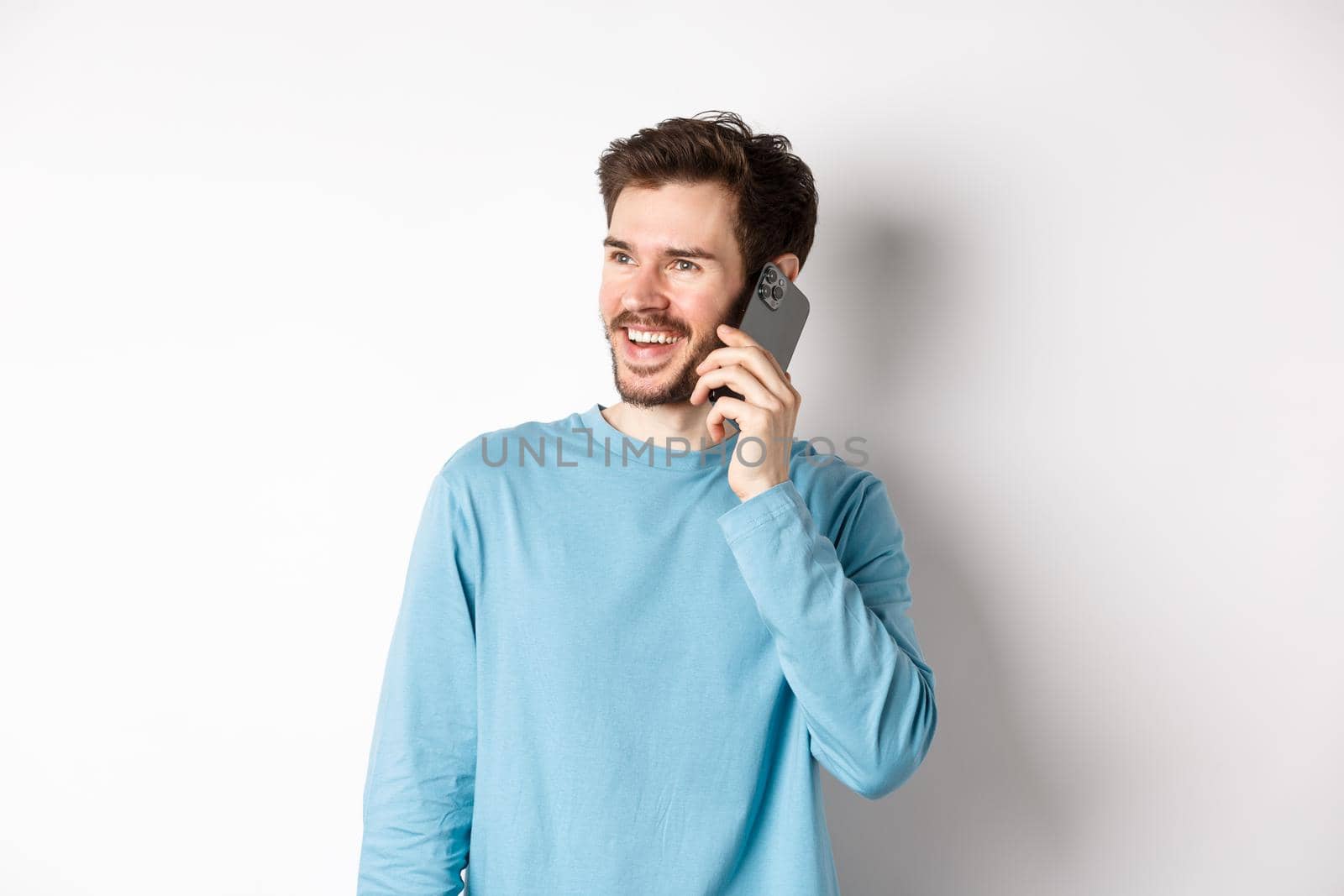 Technology concept. Joyful man enjoying phone call, talking on smartphone and smiling, standing in casual shirt over white background by Benzoix