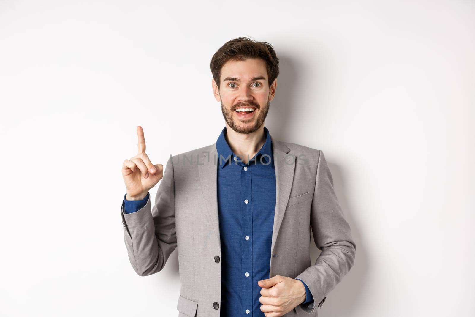 Excited businessman in suit pitching good idea, raising finger in eureka sign and looking amused, saying suggestion, standing on white background by Benzoix