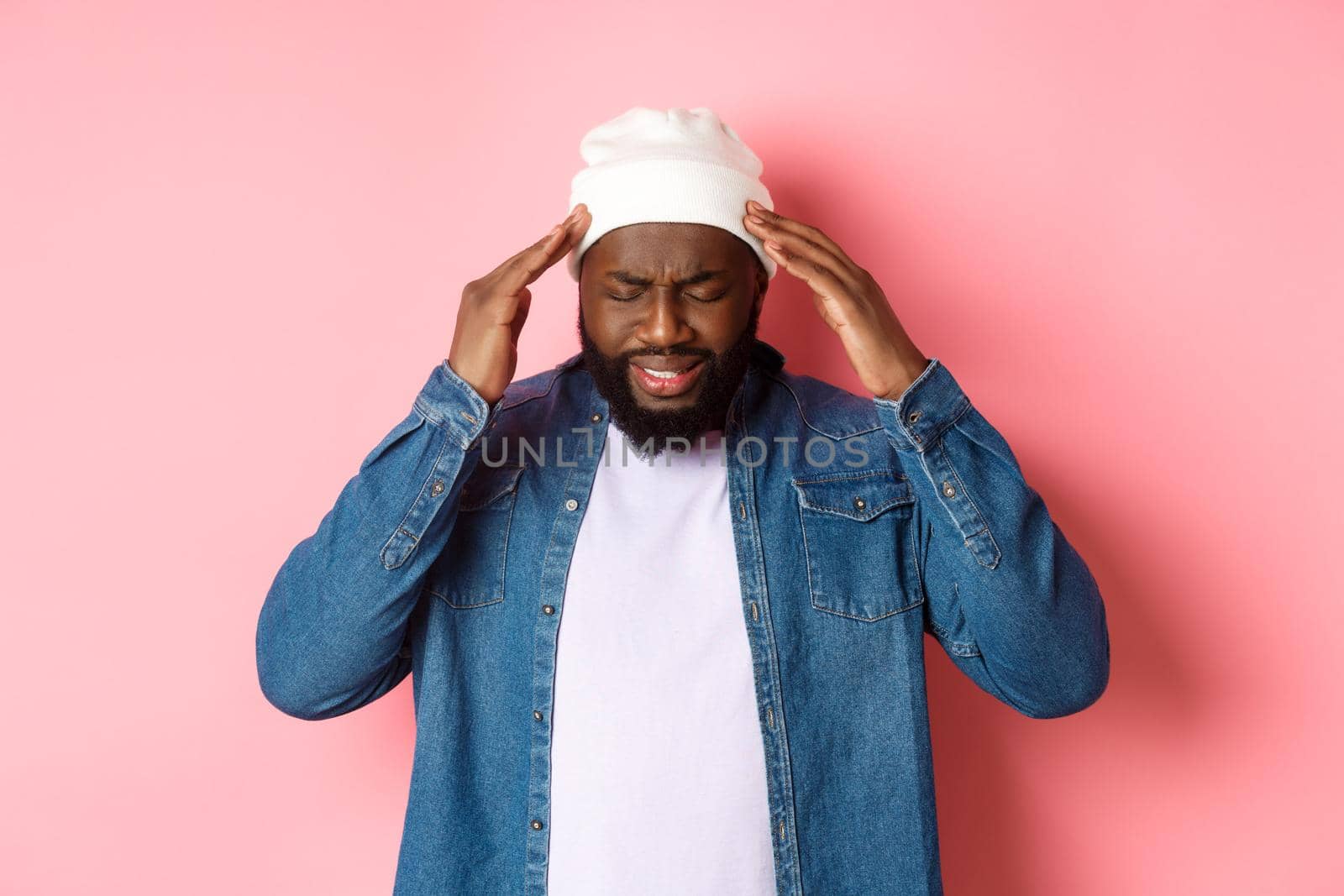 Distressed Black man having headache, touching head and grimacing with concerned face, standing over pink background.
