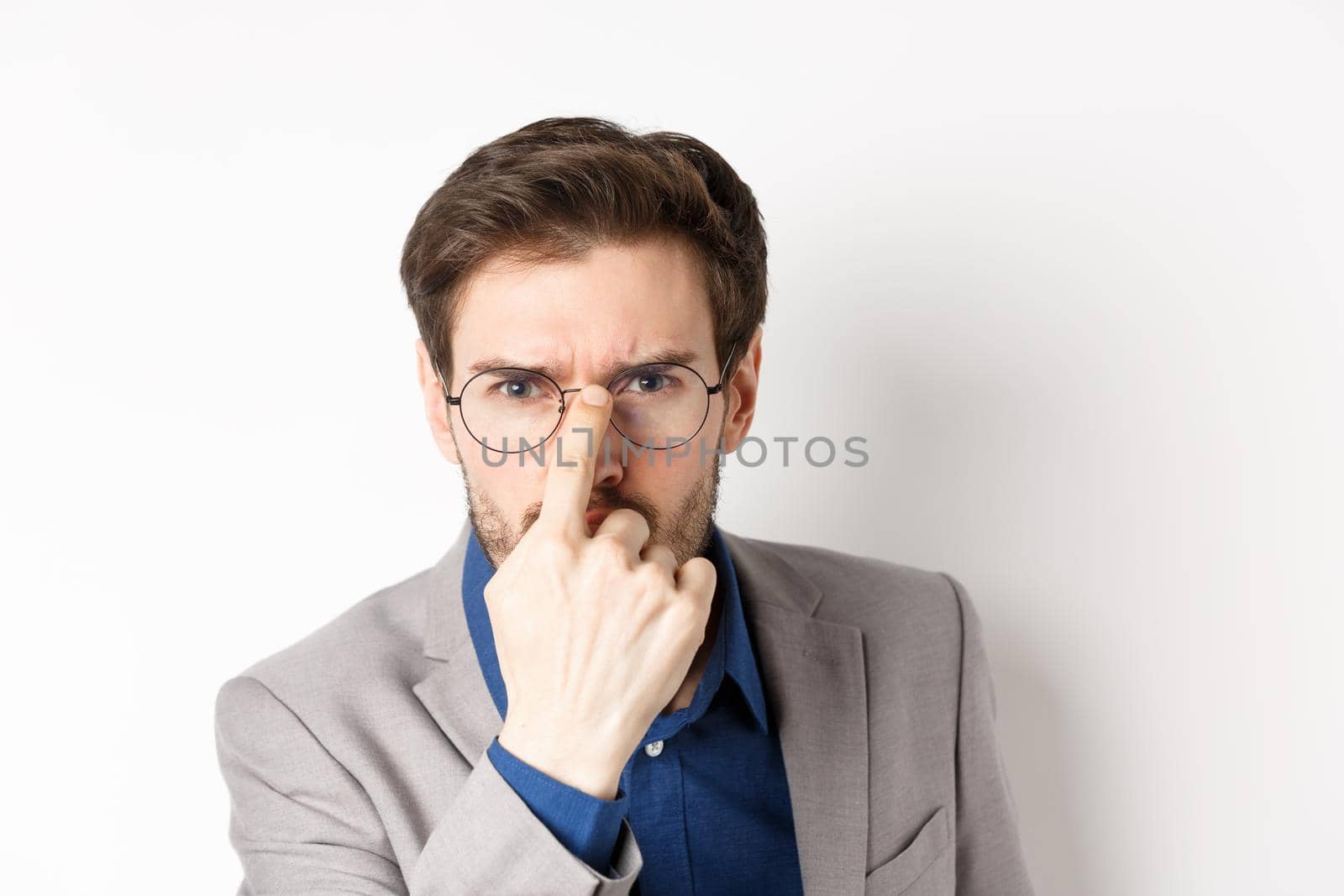 Serious boss in suit frowning, put on glasses and looking suspicious at camera, white background by Benzoix