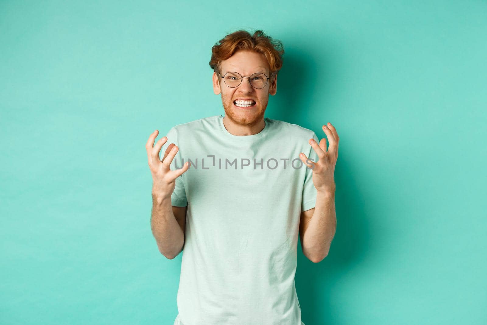 Portrait of distressed and angry redhead guy losing temper, shouting and shaking hands outraged, staring with furious face at camera, standing over mint background by Benzoix