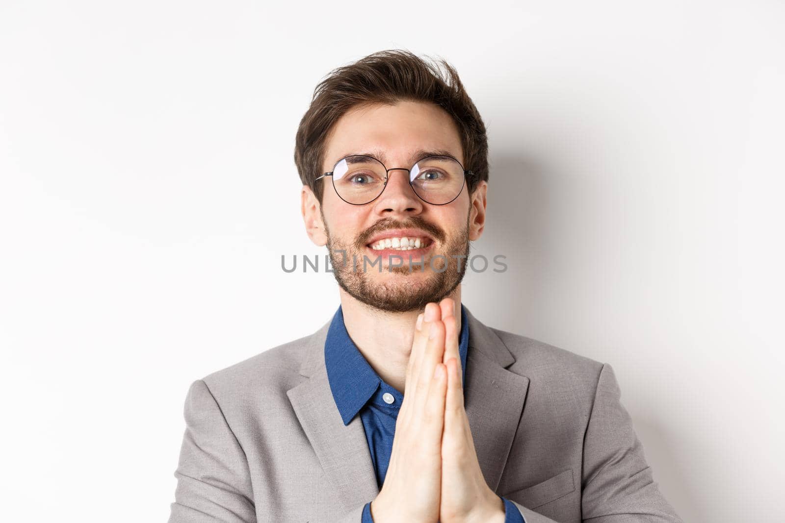 Close-up of happy thankful guy in glasses and suit showing gratitude, make namaste sign and smiling, standing on white background by Benzoix