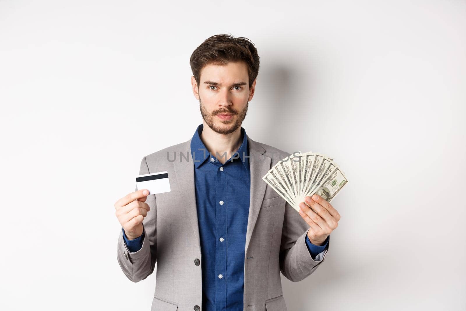 Successful businessman making money, standing in suit with dollar bills and plastic credit card, white background.