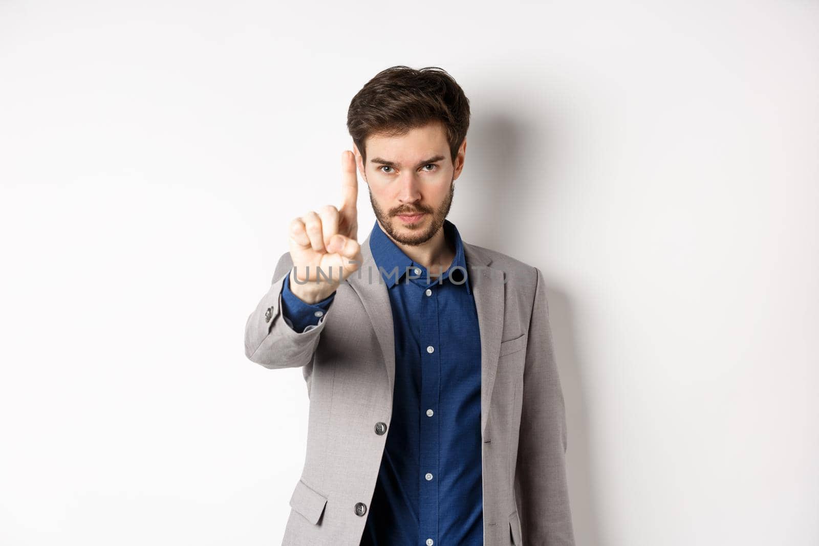 Listen to me. Serious male ceo manager showing one finger, scolding or telling to stop, tell no, hold right there sign, standing on white background in suit by Benzoix