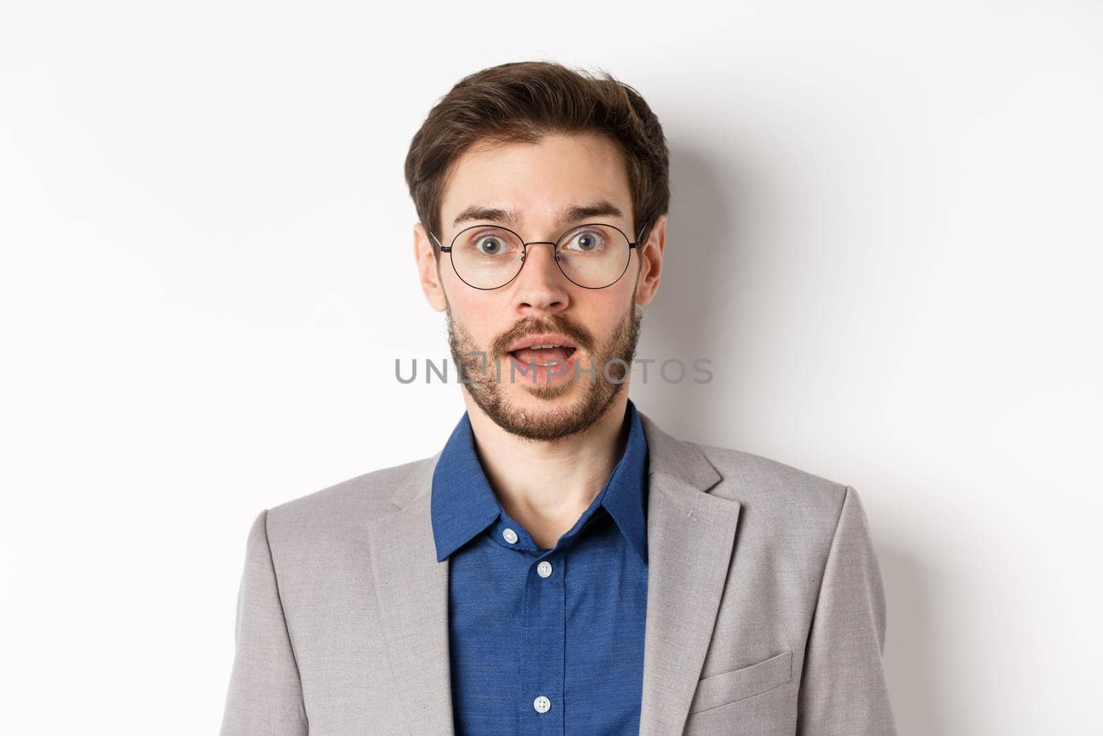 Close-up of surprised business man in glasses and suit gasping amazed, hear good news, standing on white background.