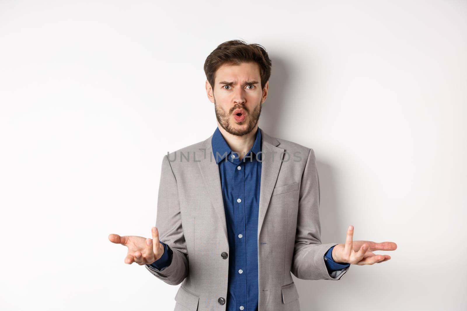 Confused and shocked businessman raising hands up and asking what happened, frowning disappointed, waiting for explanation, standing in suit on white background by Benzoix