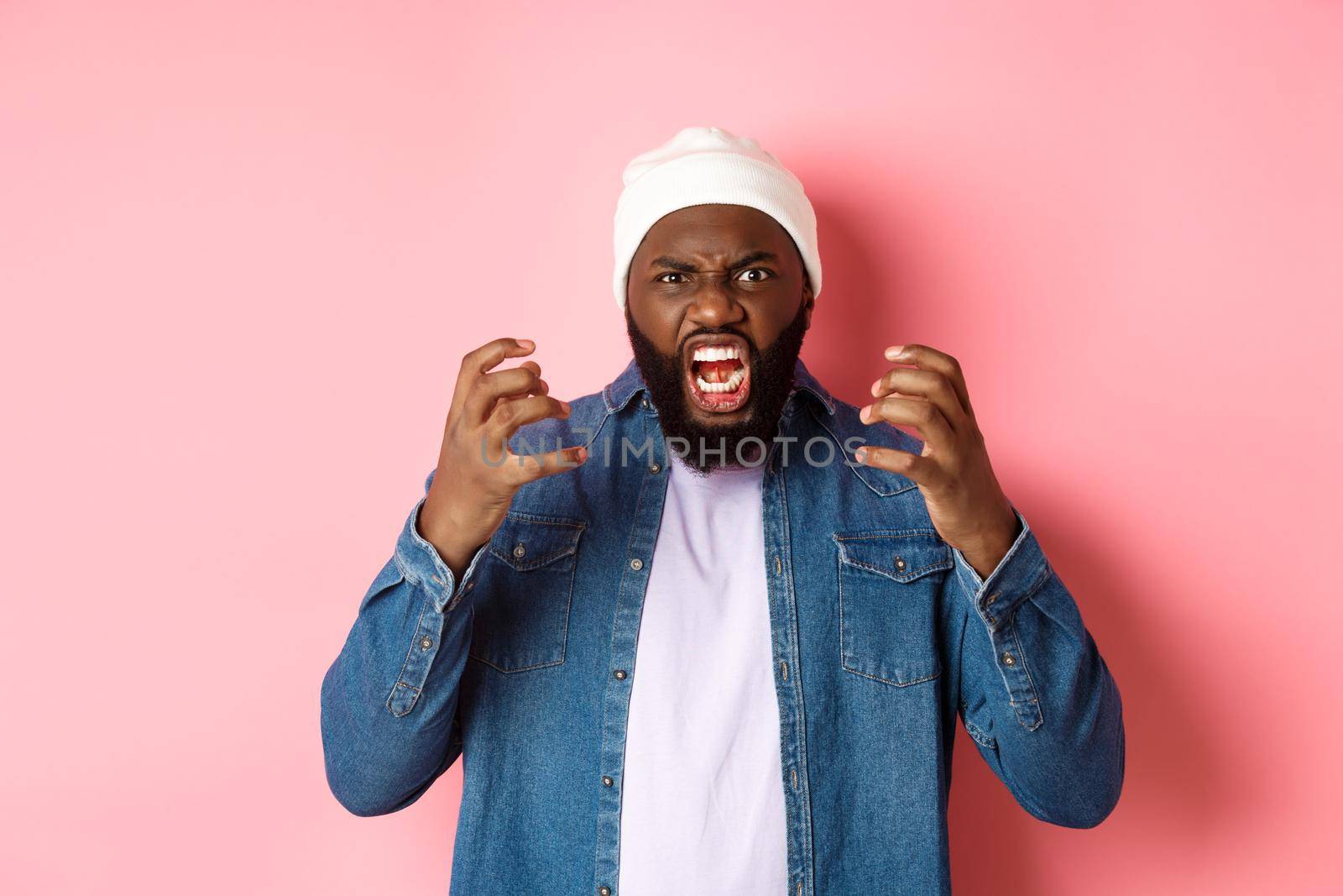 Angry african-american guy shouting and looking pissed-off, scream at camera, standing over pink background.