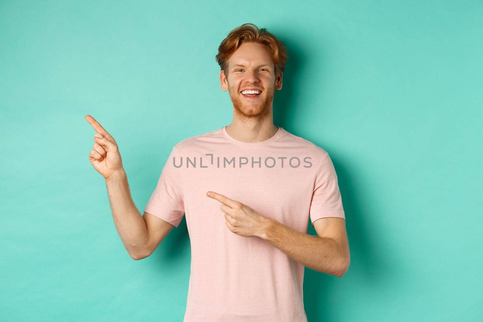 Attractive caucasian man in t-shirt pointing fingers left, smiling happy and showing advertisement, standing over turquoise background by Benzoix