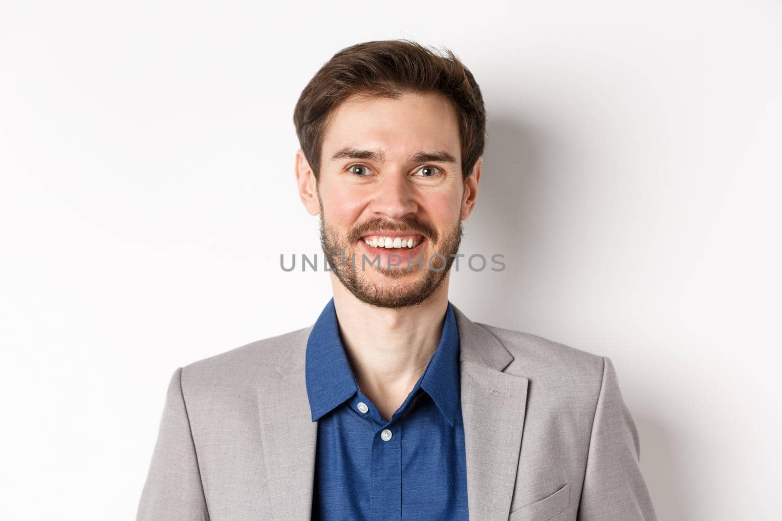 Close-up of happy bearded man in suit laughing and smiling, standing on white background.