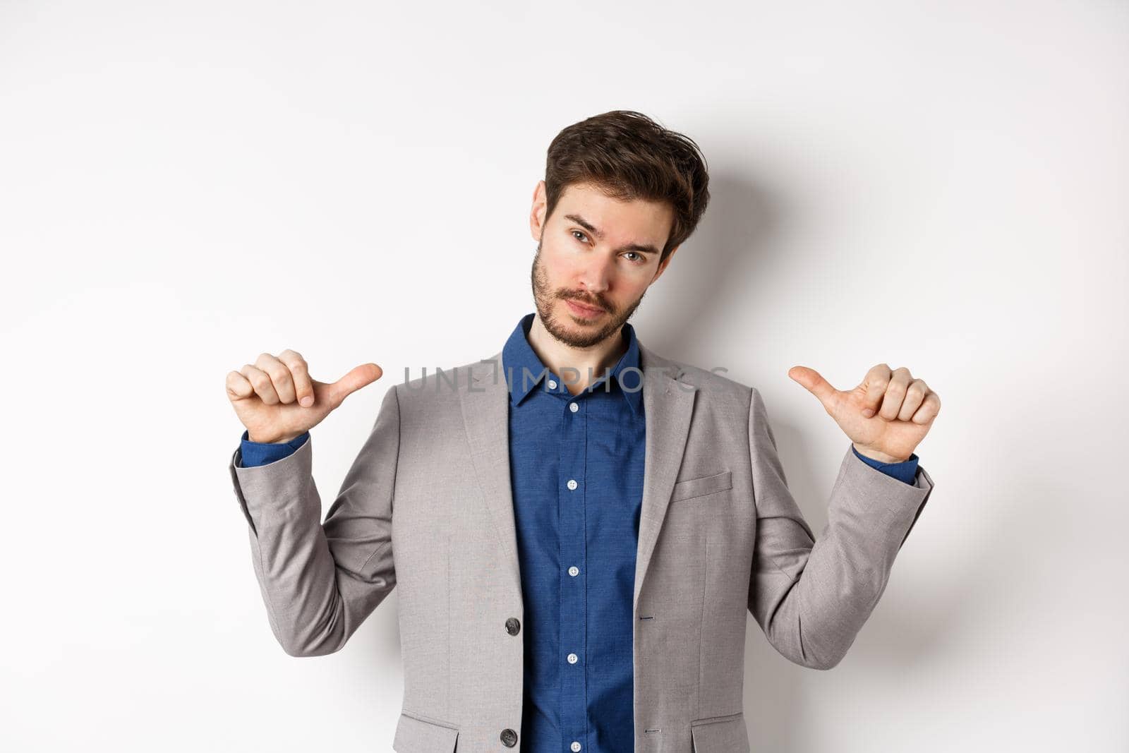 Confident man in business suit looking like professional, pointing at himself, self-promoting, standing on white background.