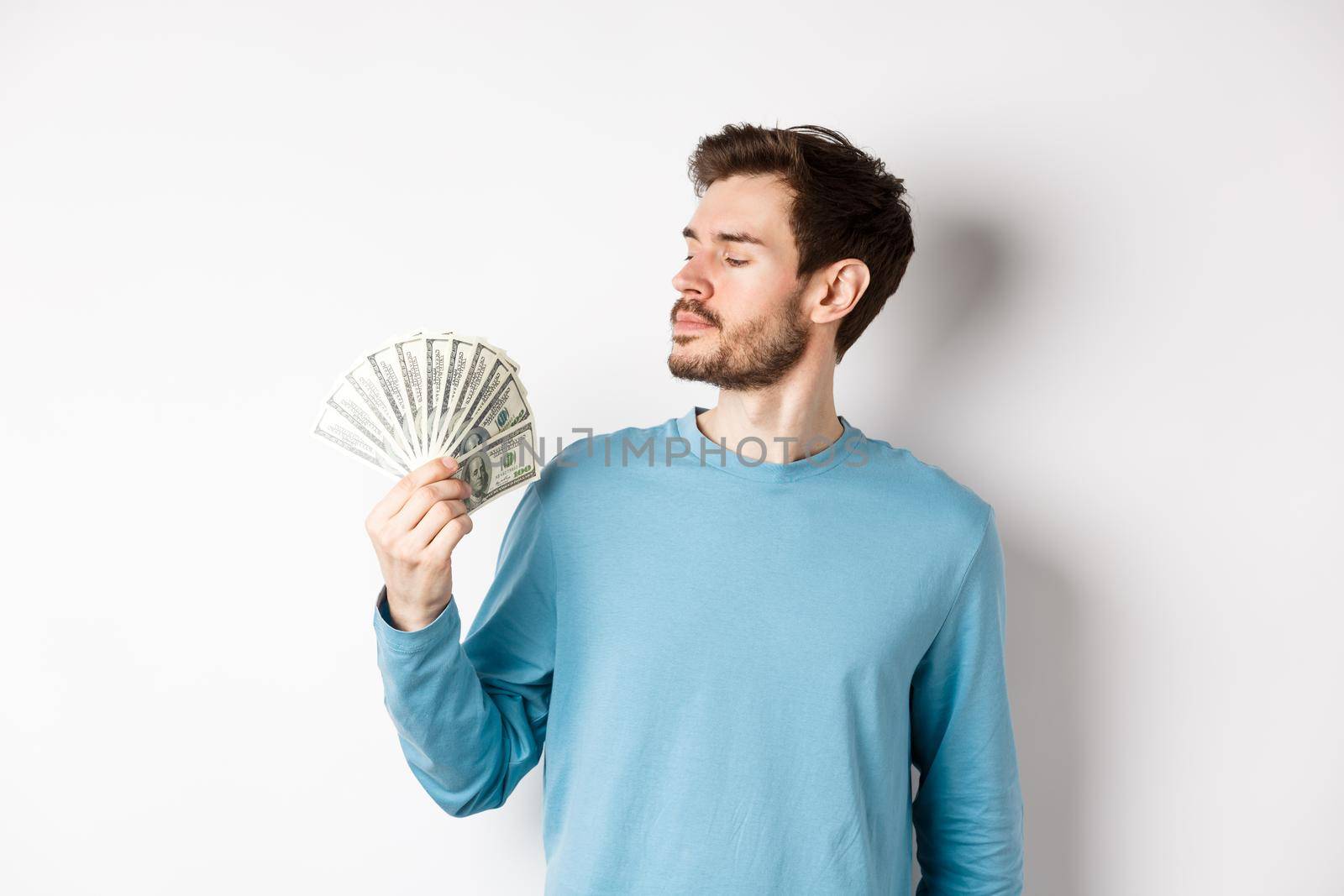 Handsome rich man with beard looking at money, got quick loan, standing over white background.