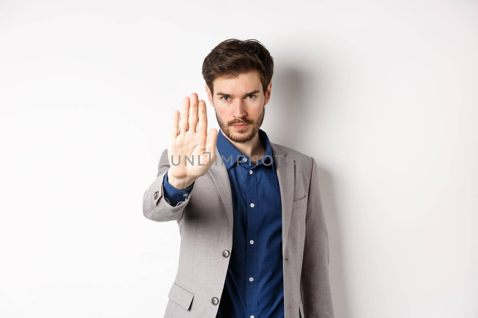 Hold right there. Serious businessman in suit stretch out hand and tell to stop, frowning and look confident, disapprove action, prohibit something bad, standing on white background.