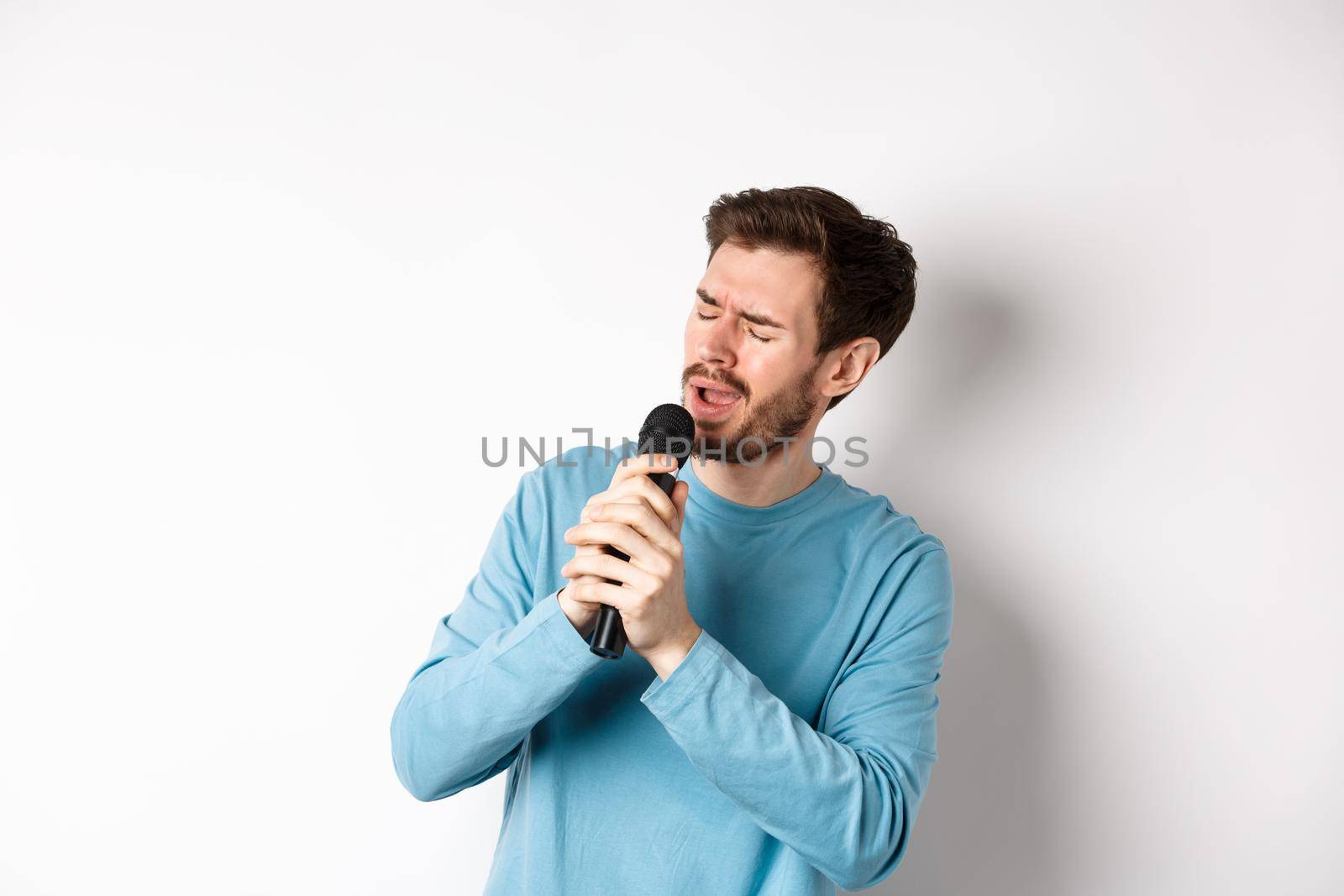 Romantic man singing song in microphone at karaoke, standing over white background by Benzoix