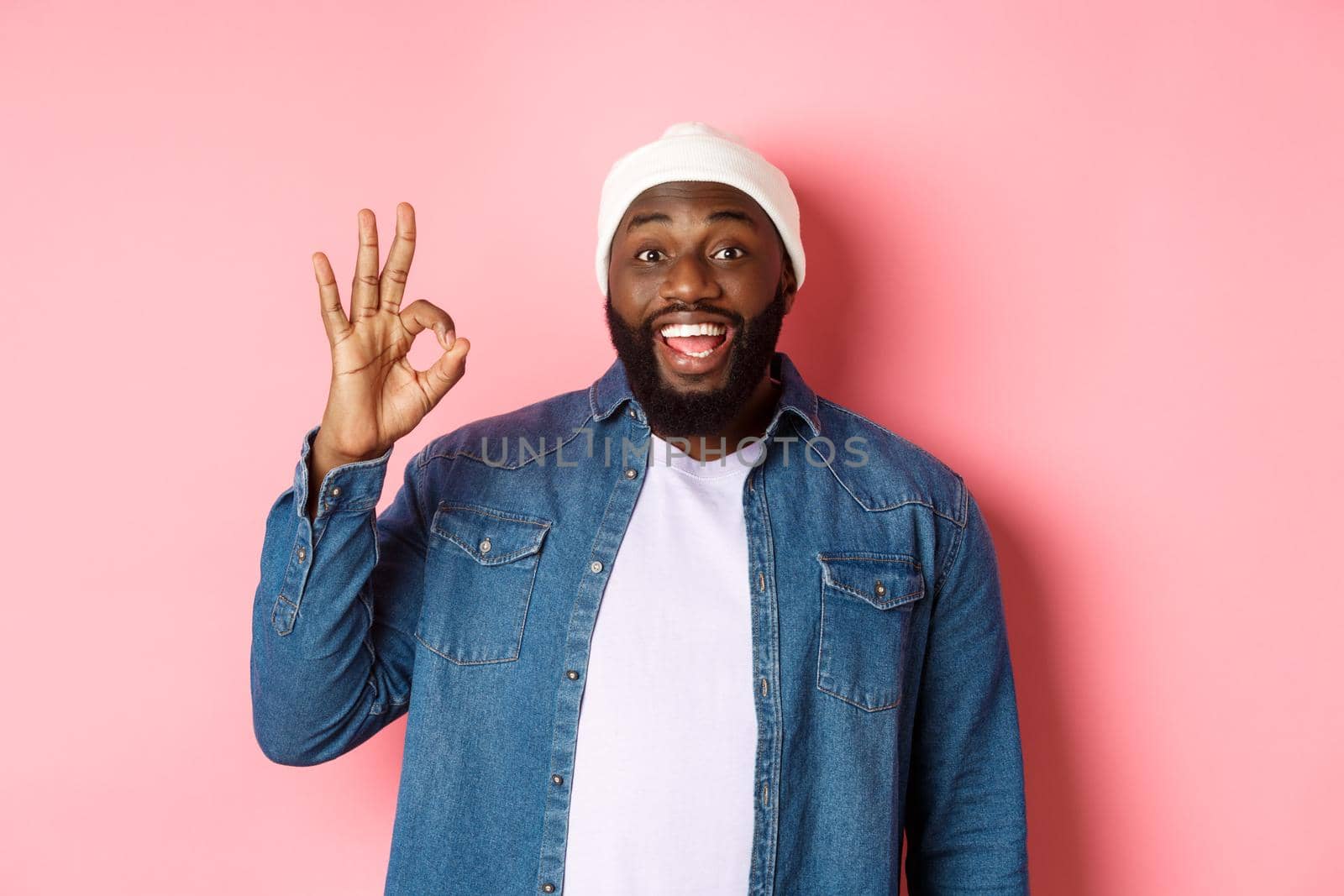 Happy smiling Black guy showing okay sign, approve and praise good offer, standing over pink background by Benzoix