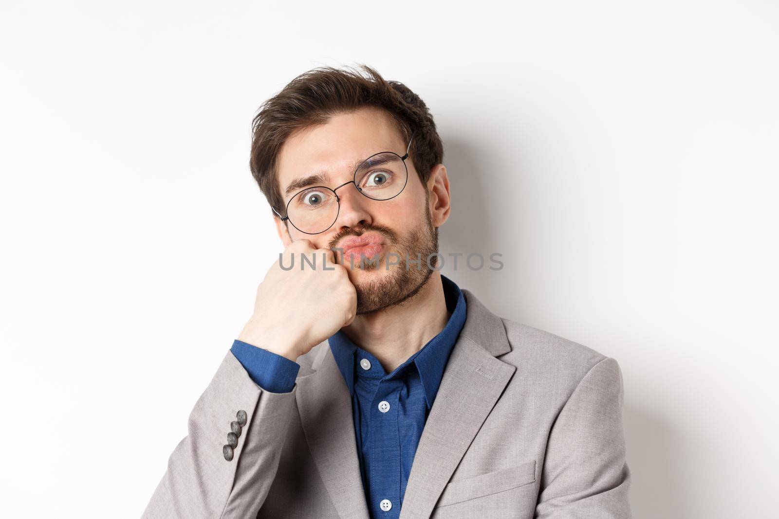 Bored funny office worker in glasses, pouting and holding breath, staring with popped eyes at camera, white background.