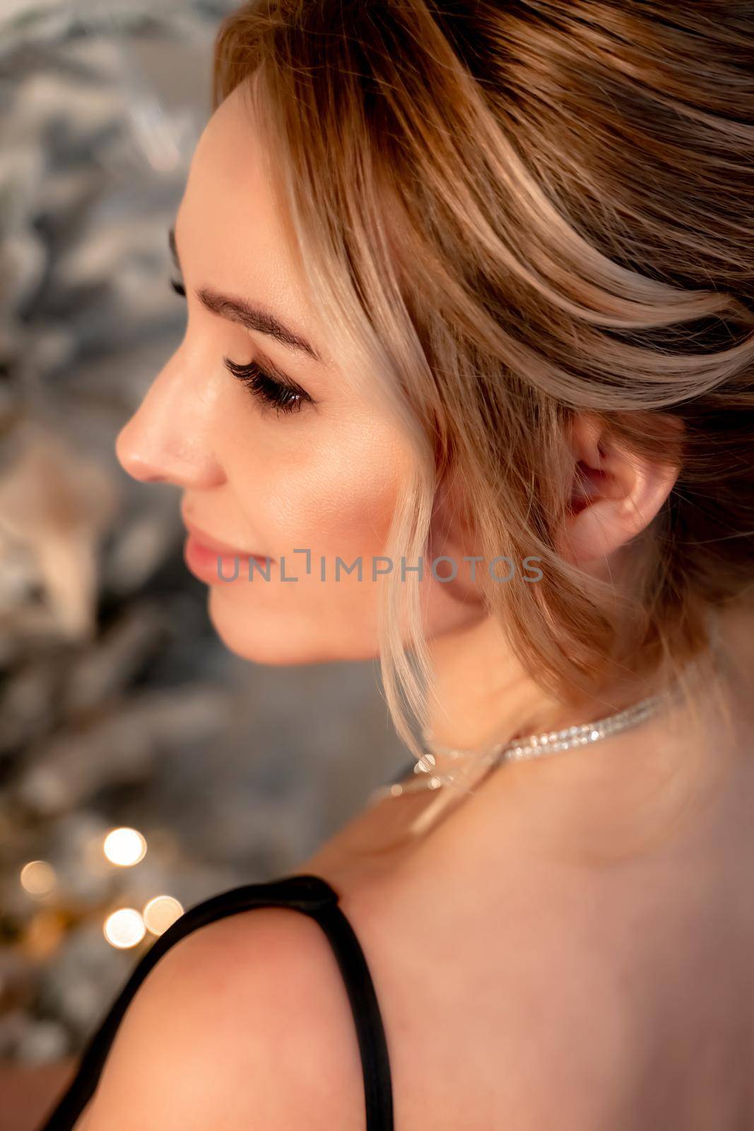 Portrait of a wealthy mature woman with evening makeup and hairstyle posing in a black dress against the backdrop of a Christmas room. Luxurious lifestyle. Cosmetology, plastic surgery, rejuvenation. by Matiunina